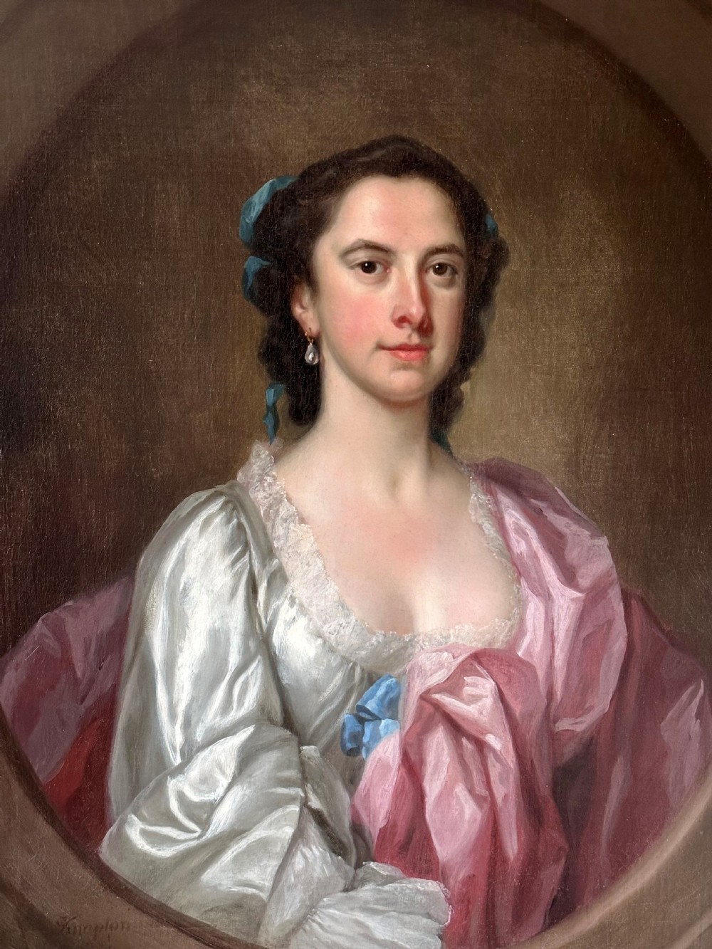 An 18th-century oil portrait of a woman in a pink and white dress set within a feigned oval and enclosed by a gold carved giltwood frame. View II