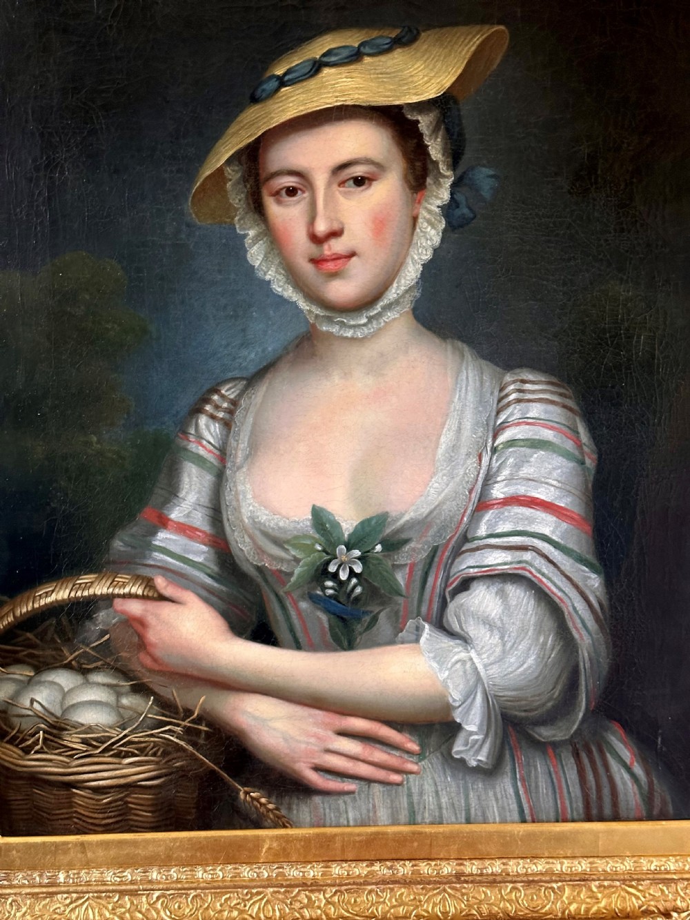 An eighteenth-century oil portrait on canvas depicting a woman in a striped dress and straw hat holding a basket of eggs, presented in an ornate giltwood frame. View II