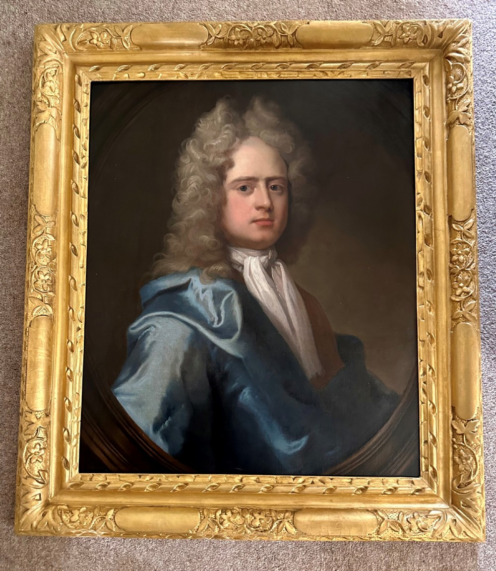 An 18th-century oil painting depicting a gentleman with a grey wig, white cravat, and blue mantle, housed within a carved gilded frame.