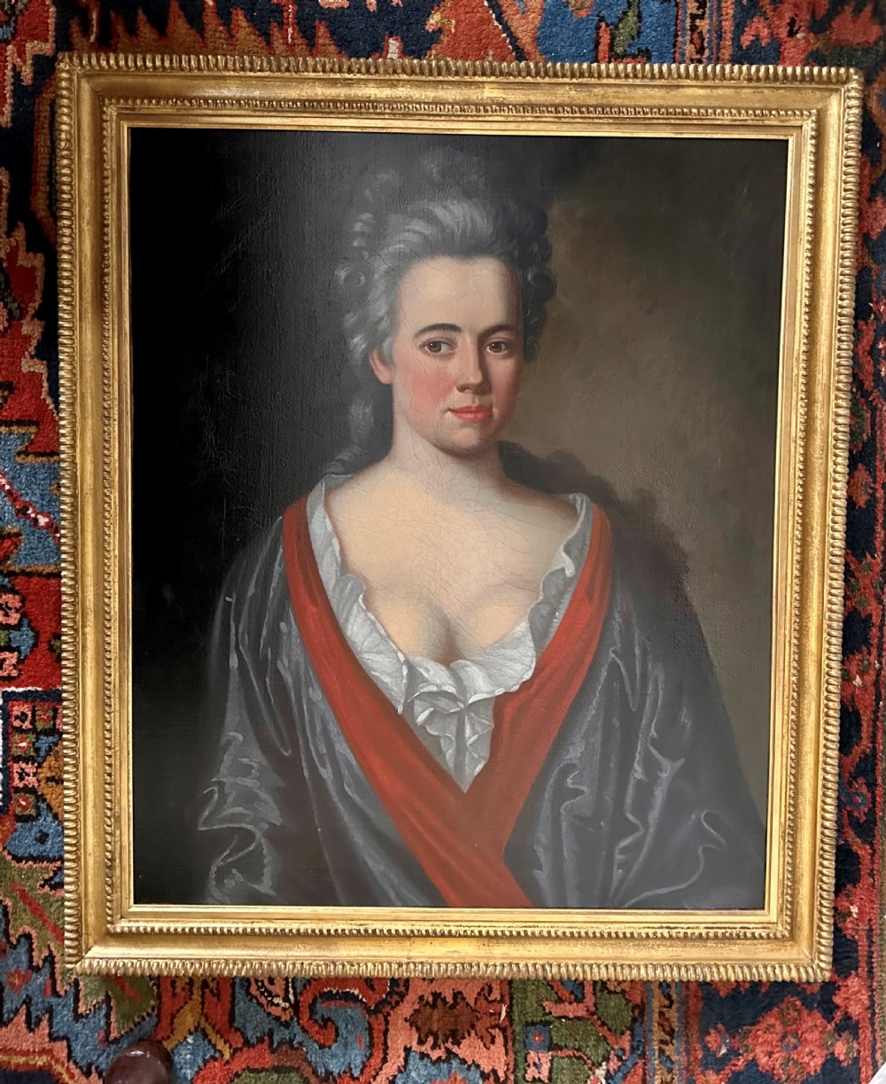 An 18th-century oil painting on canvas depicting a lady in a low-cut gown with red drapery, presented in a beaded gold leaf frame.