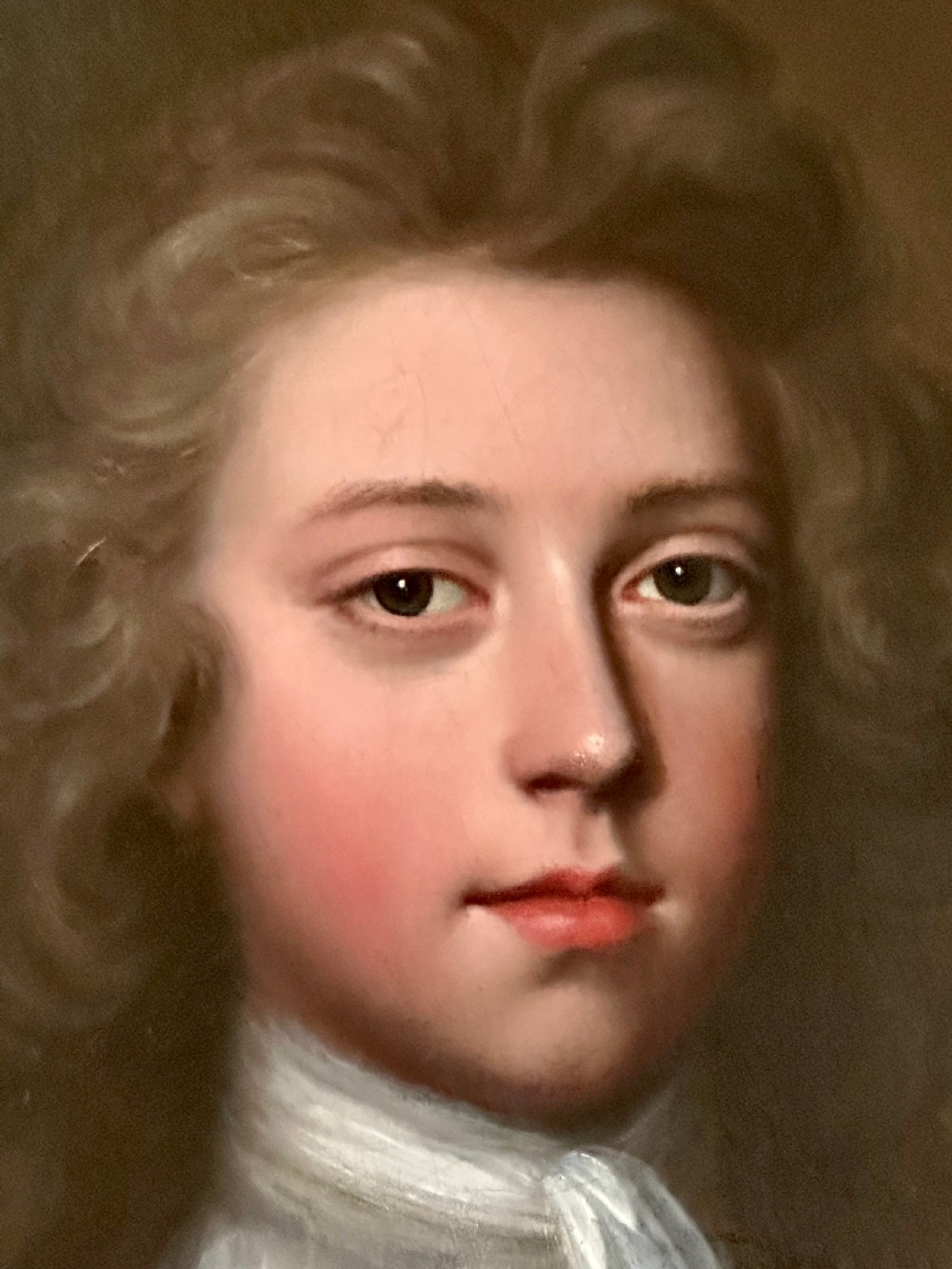 An oval 18th-century oil painting depicting a young gentleman wearing a blue coat and white cravat, set inside a carved giltwood frame. View III