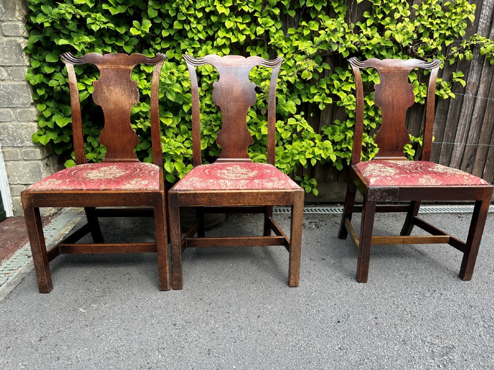 A set of three mid-18th-century Georgian mahogany side chairs featuring vasiform back splats, carved top rails, and red patterned drop-in seats.