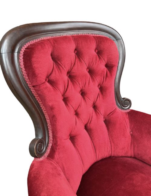 fig 1. A Victorian spoon-back armchair upholstered in crimson red button-tufted velvet with a dark carved timber frame and turned front legs on castors.