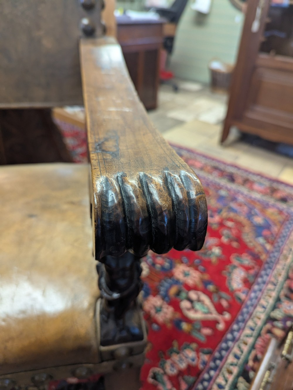 An 18th-century European walnut throne chair featuring high-backed studded leather upholstery, carved armrests, finials, and an ornate lower stretcher. View VI