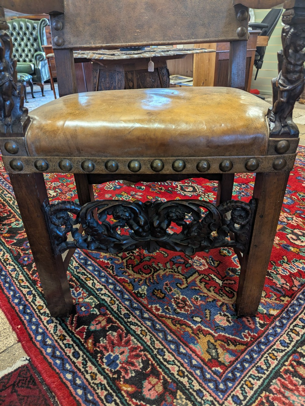 An 18th-century European walnut throne chair featuring high-backed studded leather upholstery, carved armrests, finials, and an ornate lower stretcher. View VII