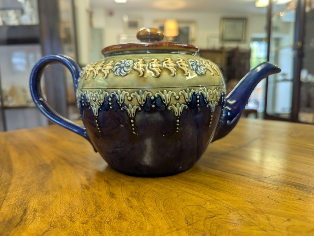 An Art Nouveau Royal Doulton stoneware teapot featuring a cobalt blue base, an olive green shoulder with raised relief patterns, and a fitted lid.