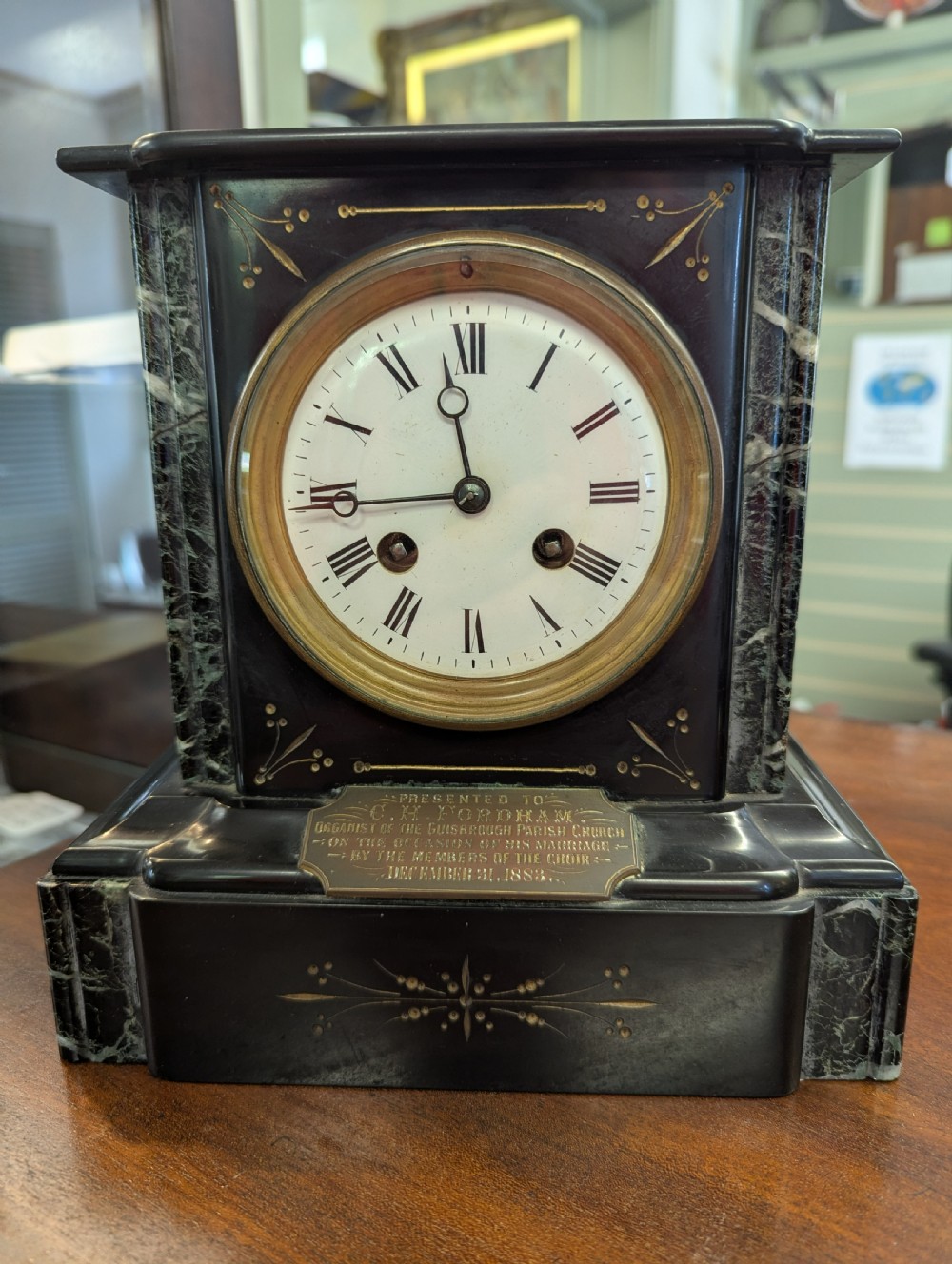 A Victorian black marble and slate mantel clock featuring incised gilded floral patterns, a white enamel dial with Roman numerals, and a brass presentation plaque.