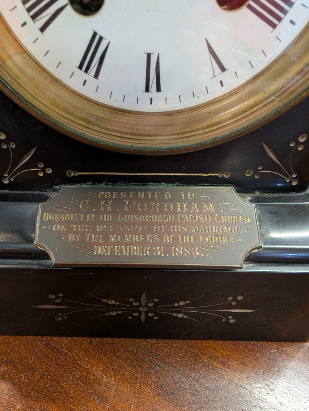A Victorian black marble and slate mantel clock featuring incised gilded floral patterns, a white enamel dial with Roman numerals, and a brass presentation plaque. View III