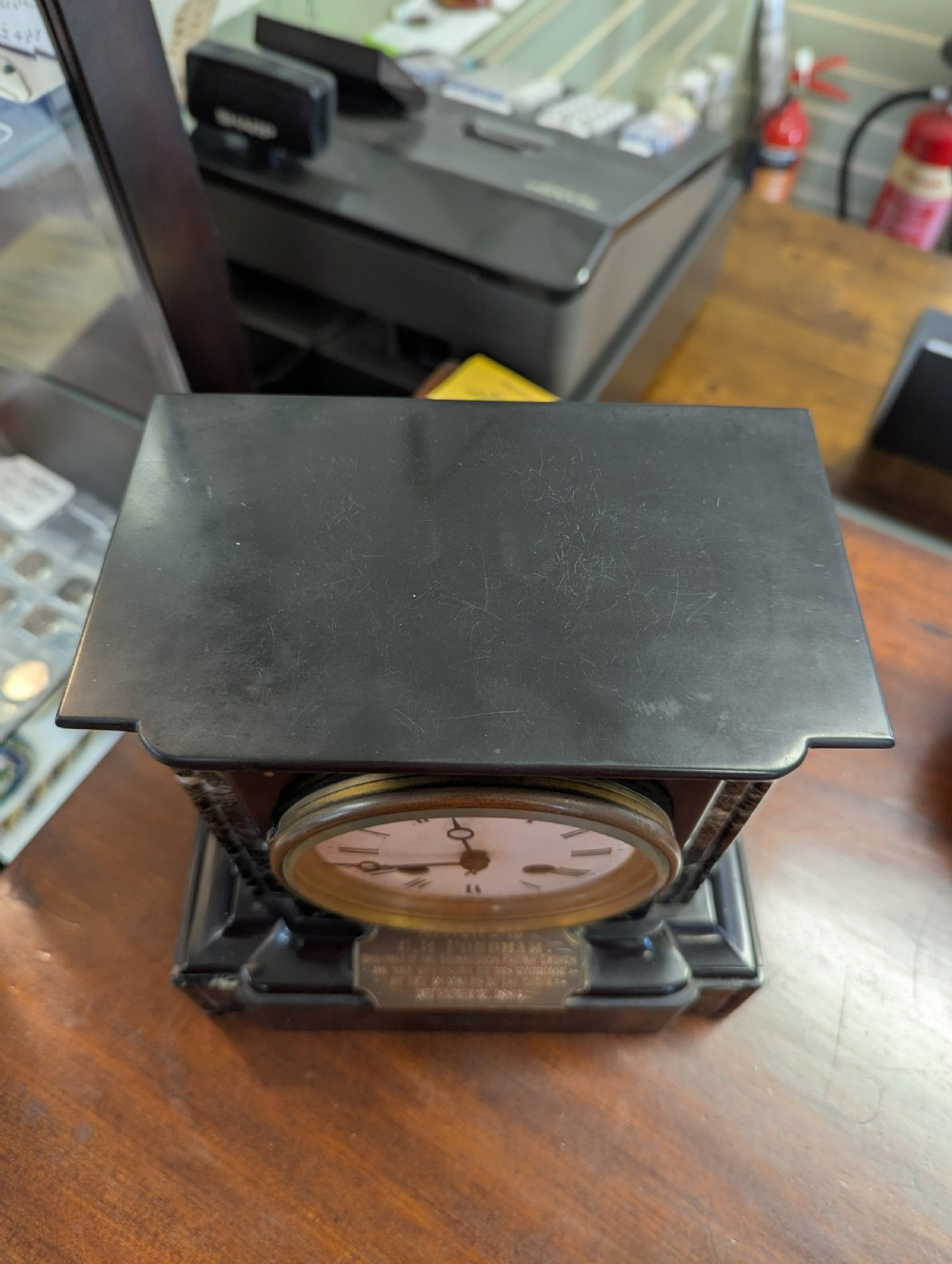 A Victorian black marble and slate mantel clock featuring incised gilded floral patterns, a white enamel dial with Roman numerals, and a brass presentation plaque. View VI