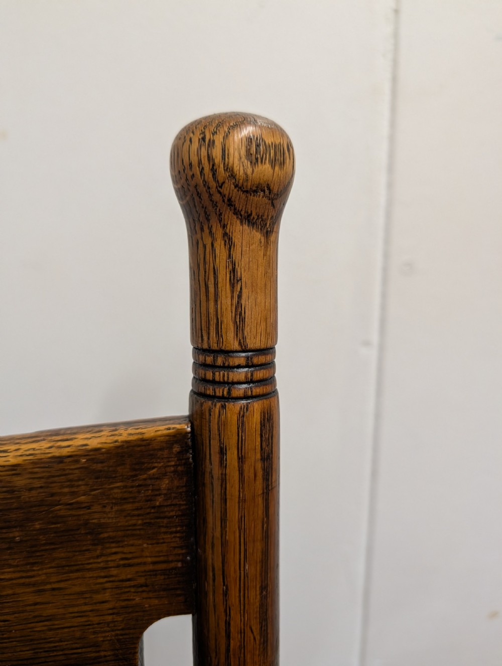 An Arts and Crafts oak open armchair featuring curved sweeping arms, a shaped timber backboard, turned legs with double stretchers, and an inset brown leather seat fixed with brass studs. View V