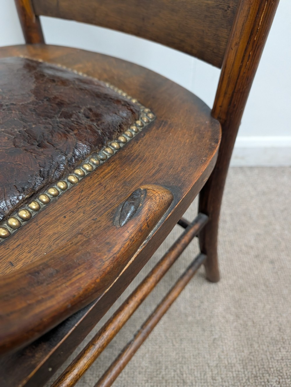 An Arts and Crafts oak open armchair featuring curved sweeping arms, a shaped timber backboard, turned legs with double stretchers, and an inset brown leather seat fixed with brass studs. View VIII