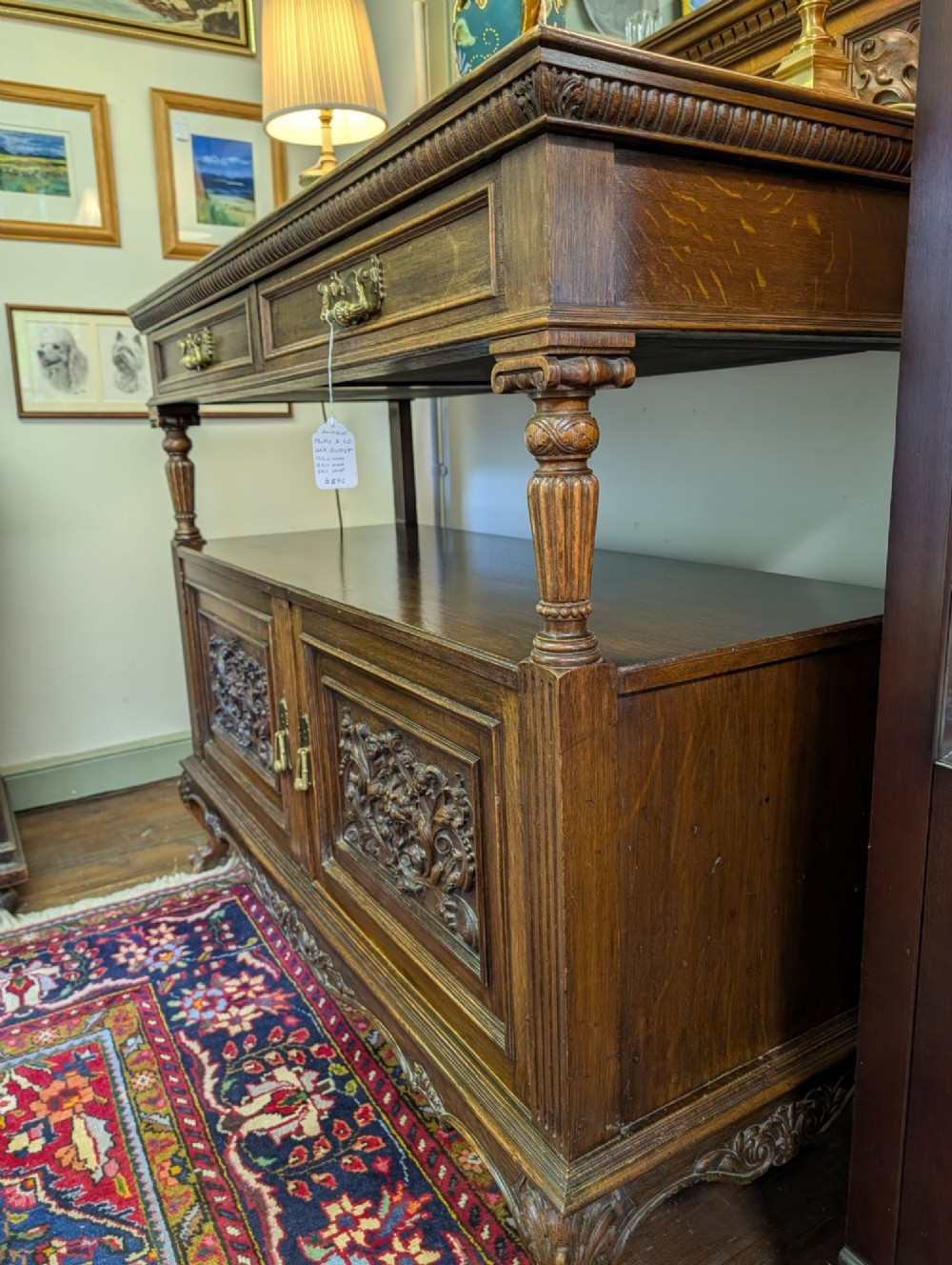 A late Victorian carved oak buffet featuring two top drawers with brass drop handles, an open tier, and a lower double-door cabinet decorated with detailed carved foliage. View III