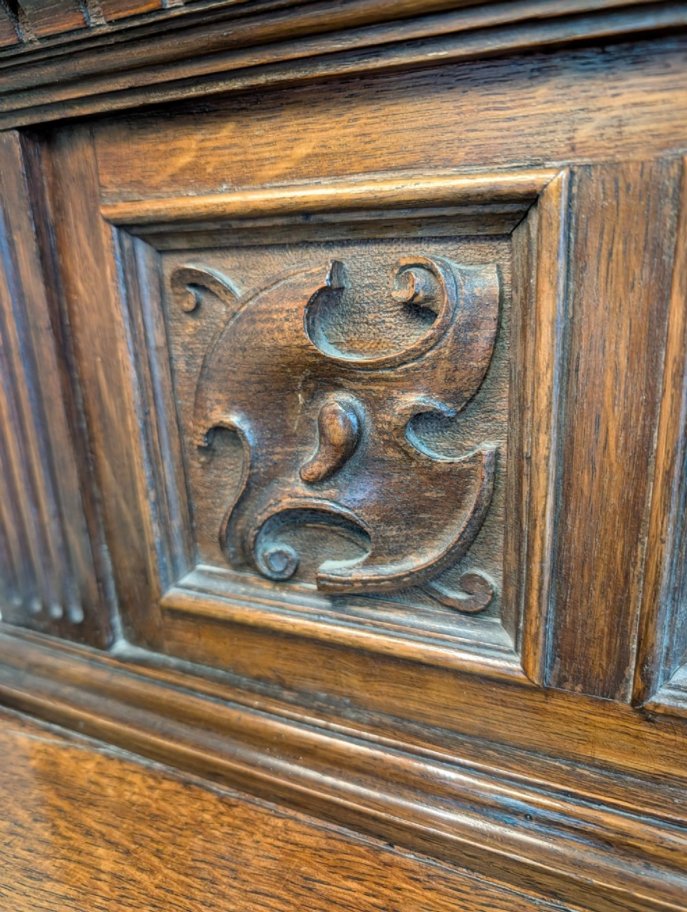 A late Victorian carved oak buffet featuring two top drawers with brass drop handles, an open tier, and a lower double-door cabinet decorated with detailed carved foliage. View IV