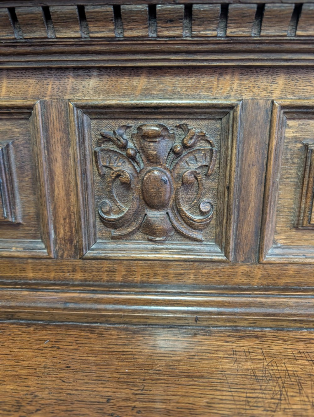 A late Victorian carved oak buffet featuring two top drawers with brass drop handles, an open tier, and a lower double-door cabinet decorated with detailed carved foliage. View V