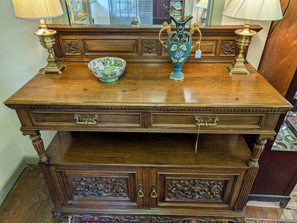 A late Victorian carved oak buffet featuring two top drawers with brass drop handles, an open tier, and a lower double-door cabinet decorated with detailed carved foliage. View VII
