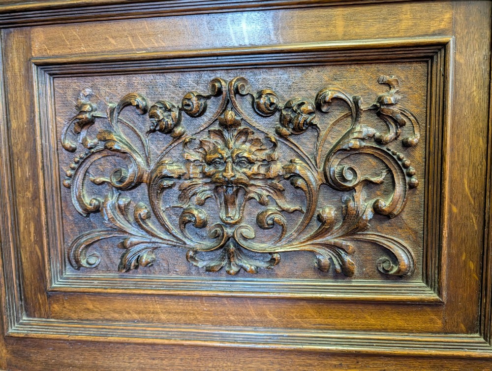 A late Victorian carved oak buffet featuring two top drawers with brass drop handles, an open tier, and a lower double-door cabinet decorated with detailed carved foliage. View XII
