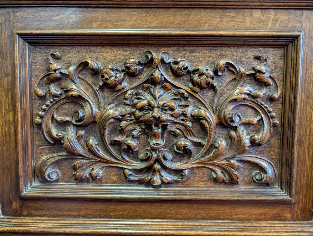 A late Victorian carved oak buffet featuring two top drawers with brass drop handles, an open tier, and a lower double-door cabinet decorated with detailed carved foliage. View XIII