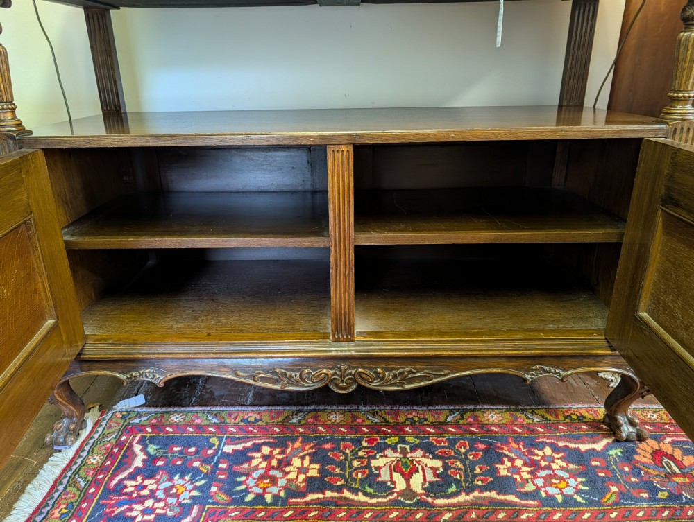 A late Victorian carved oak buffet featuring two top drawers with brass drop handles, an open tier, and a lower double-door cabinet decorated with detailed carved foliage. View XIV