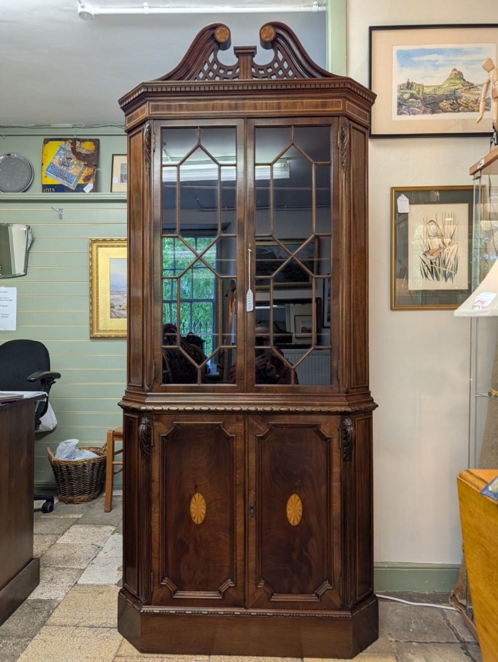 An Edwardian mahogany corner display cabinet featuring a swan-neck pediment, astragal glazed top doors, and lower inlaid timber panelled doors.