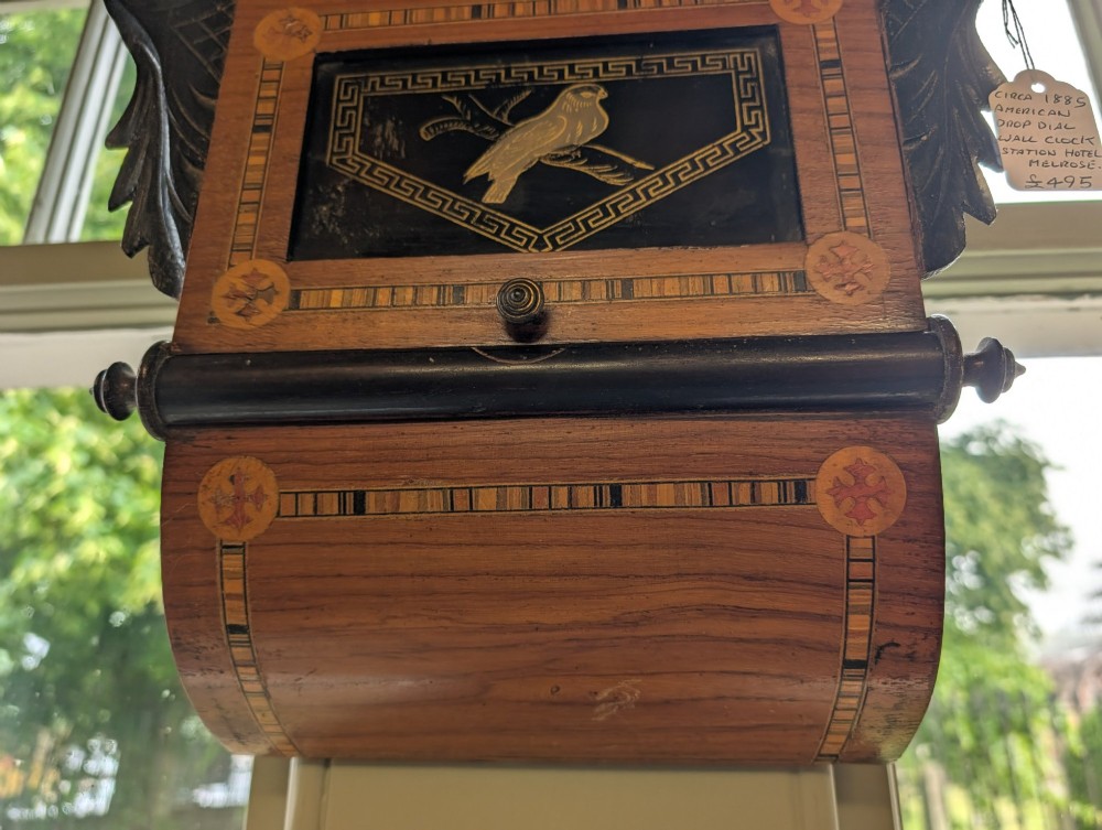 A 19th-century American drop dial wall clock made of inlaid wood with a cream dial, Roman numerals, and a glass-fronted lower panel featuring a bird design. View II