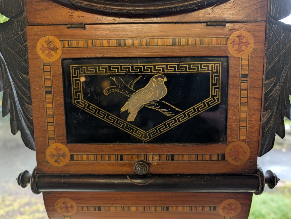A 19th-century American drop dial wall clock made of inlaid wood with a cream dial, Roman numerals, and a glass-fronted lower panel featuring a bird design. View III