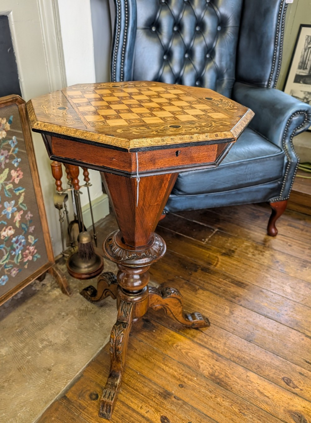 A Victorian octagonal walnut games table featuring an inlaid chessboard lid above a tapering trumpet pedestal on carved tripod legs.