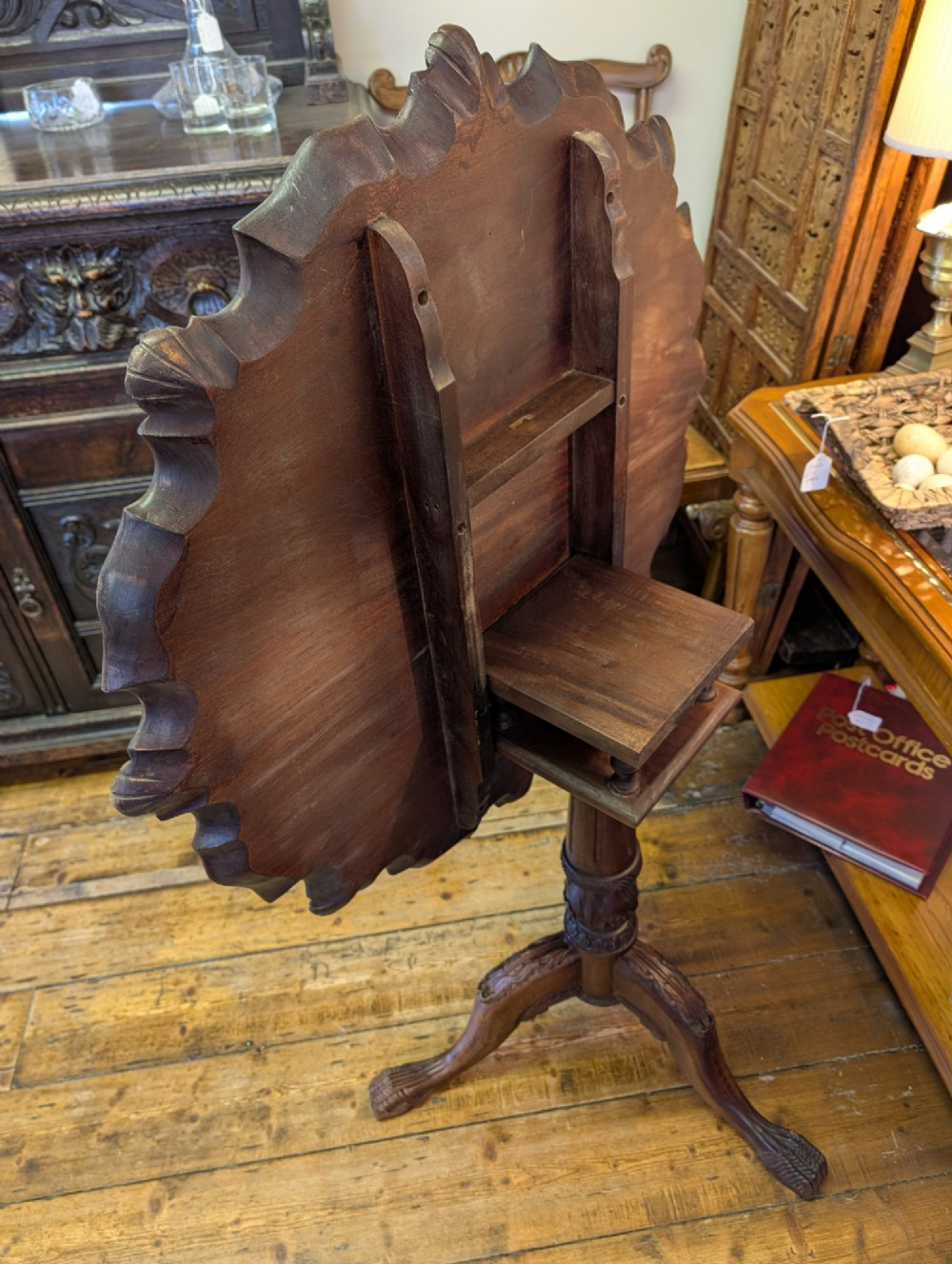 A top-down view of a 19th-century mahogany tilt-top table featuring a carved scalloped edge with shell motifs on a central turned pedestal base. View VII