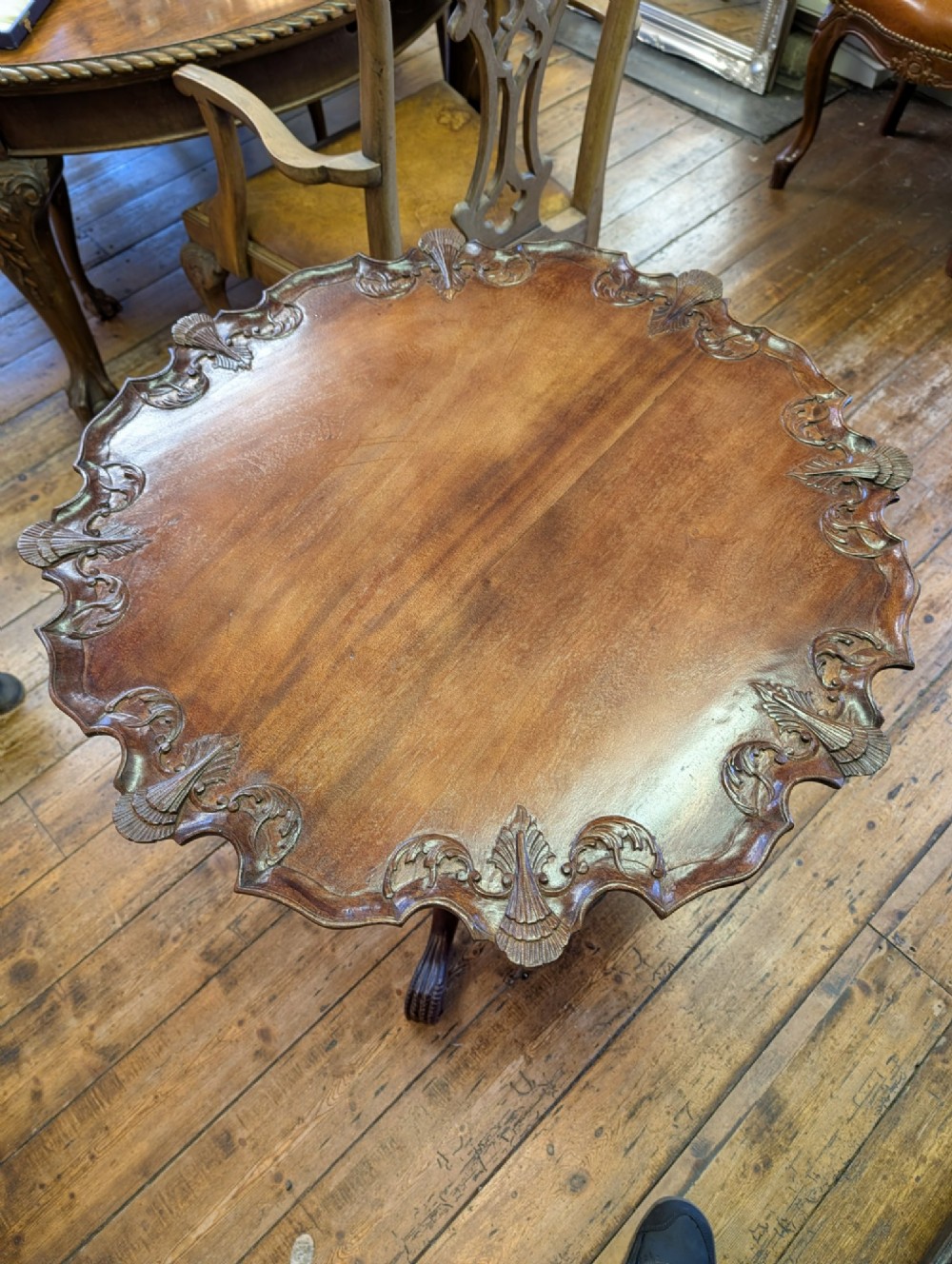 A top-down view of a 19th-century mahogany tilt-top table featuring a carved scalloped edge with shell motifs on a central turned pedestal base.