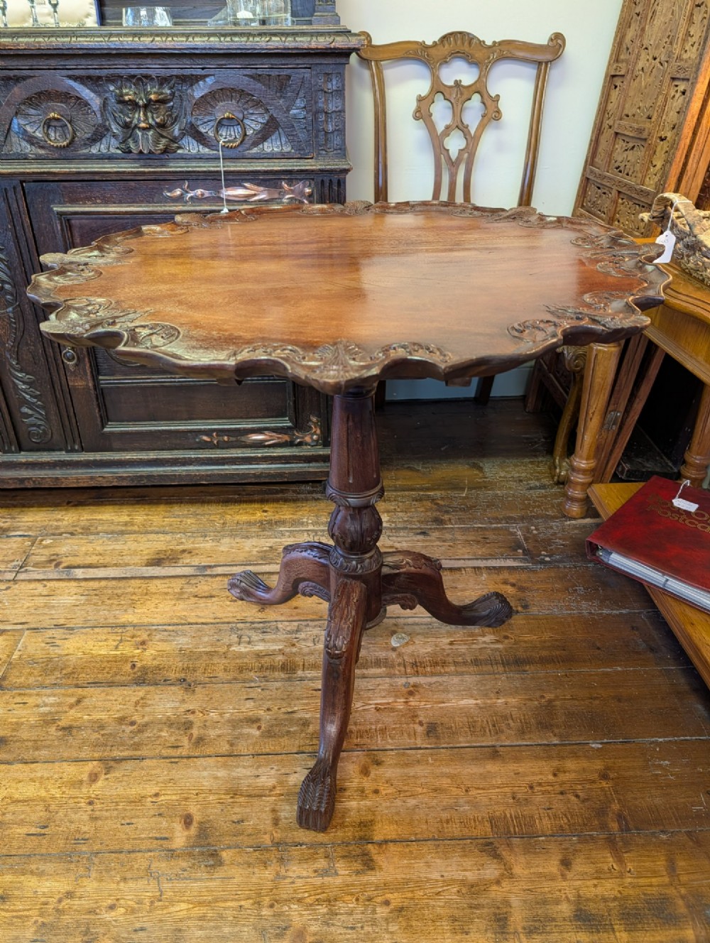 A top-down view of a 19th-century mahogany tilt-top table featuring a carved scalloped edge with shell motifs on a central turned pedestal base. View XI