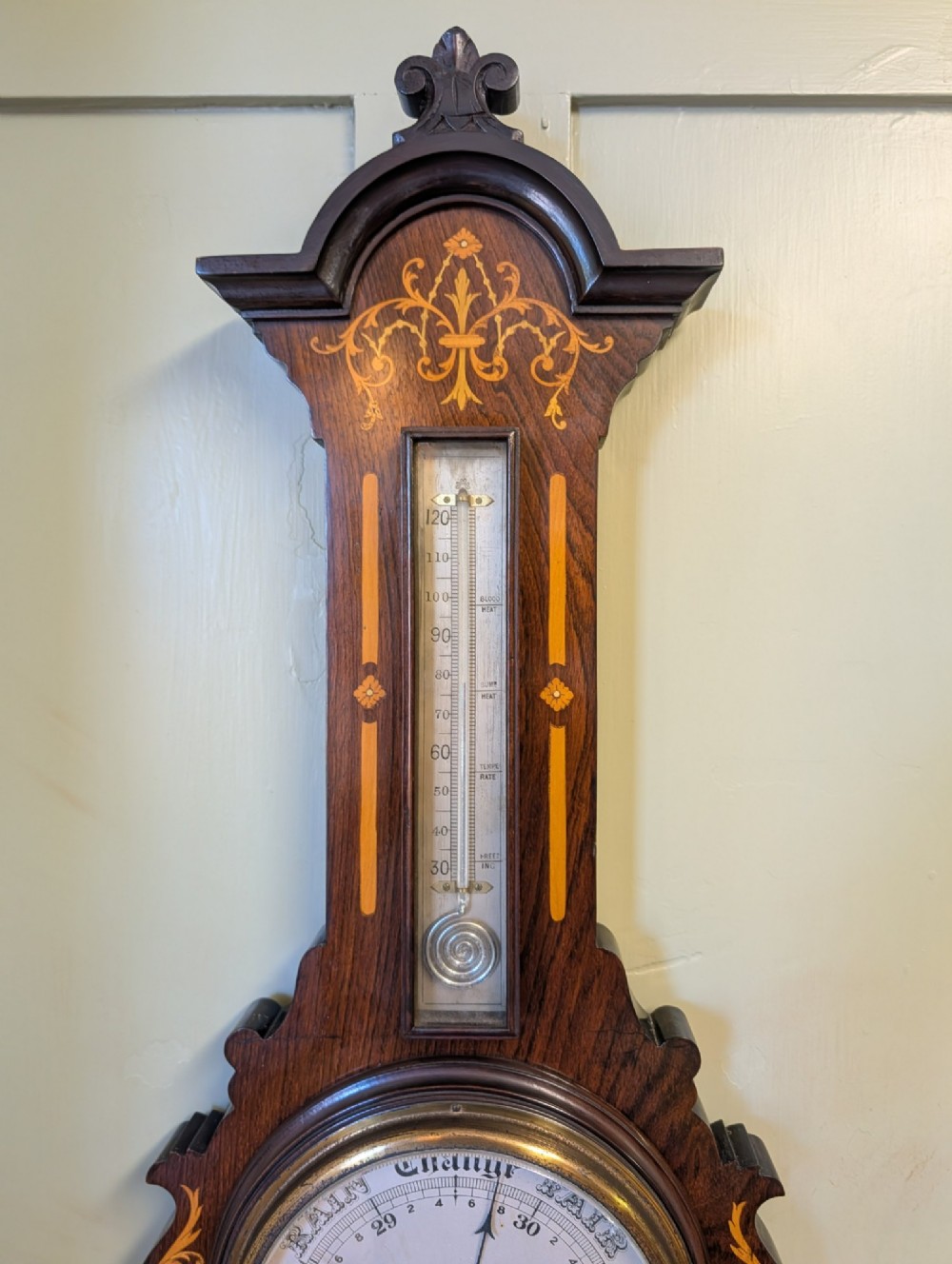 An Edwardian wall-mounted rosewood barometer featuring floral marquetry inlay, a top-mounted glass thermometer, and a circular brass-rimmed pressure dial. View III