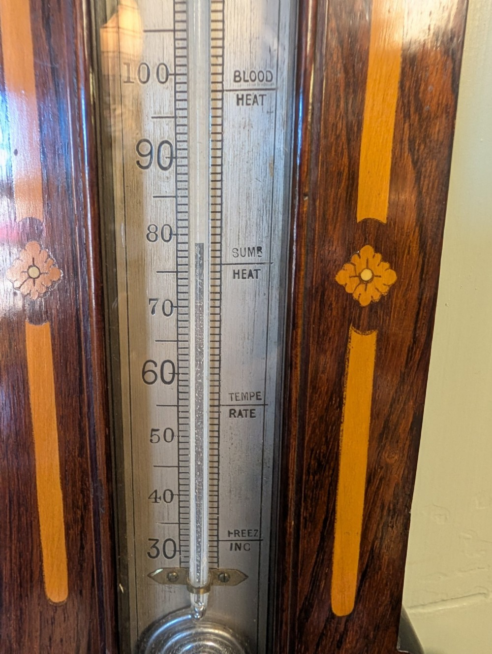 An Edwardian wall-mounted rosewood barometer featuring floral marquetry inlay, a top-mounted glass thermometer, and a circular brass-rimmed pressure dial. View IV