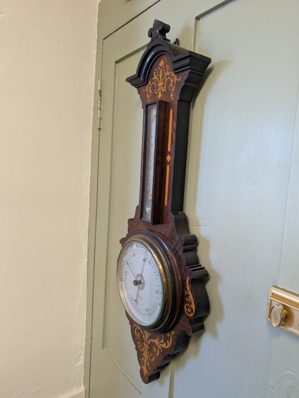 An Edwardian wall-mounted rosewood barometer featuring floral marquetry inlay, a top-mounted glass thermometer, and a circular brass-rimmed pressure dial. View V