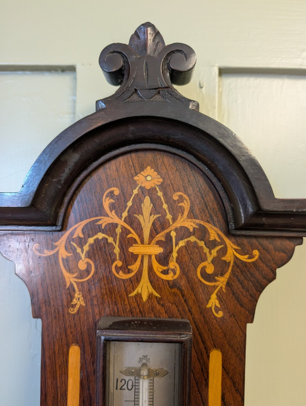 An Edwardian wall-mounted rosewood barometer featuring floral marquetry inlay, a top-mounted glass thermometer, and a circular brass-rimmed pressure dial. View VI