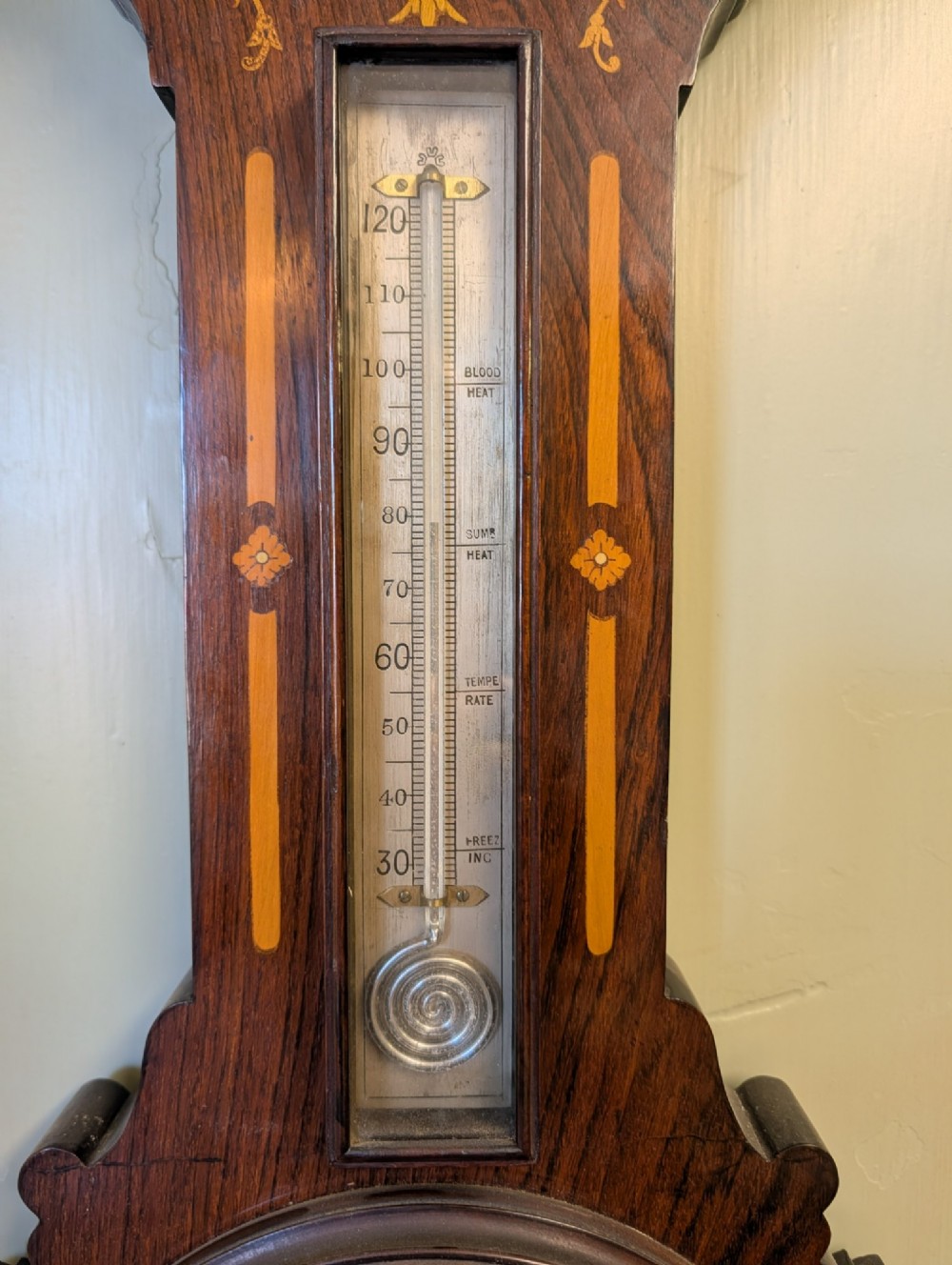 An Edwardian wall-mounted rosewood barometer featuring floral marquetry inlay, a top-mounted glass thermometer, and a circular brass-rimmed pressure dial. View XI