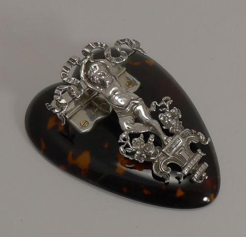 fig 1. A heart-shaped tortoiseshell letter clip mounted with sterling silver featuring a winged cherub figure and ribbon motif.