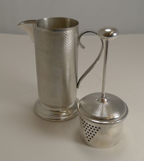 fig 1. An Art Deco silver-plated cocktail mixer featuring an engine-turned textured body, a curved side handle, a pouring spout, and a lid topped with a spherical finial.