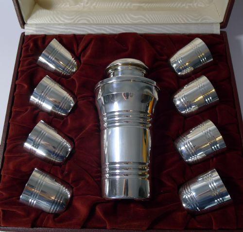 fig 1. A silver-plated Art Deco cocktail shaker and eight matching cups housed within an open burgundy velvet and cream satin fitted case.