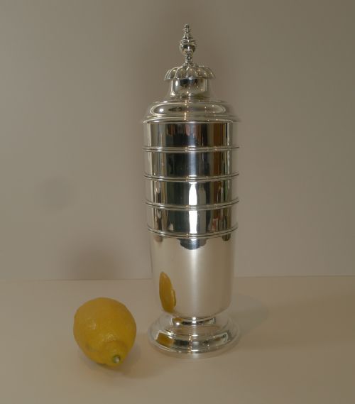 fig 1. A tall, polished sterling silver cocktail shaker featuring horizontal ribbed banding, a stepped base, and a decorative finial cap.