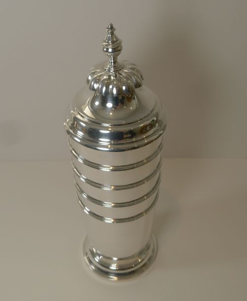 fig 2. A tall, polished sterling silver cocktail shaker featuring horizontal ribbed banding, a stepped base, and a decorative finial cap.