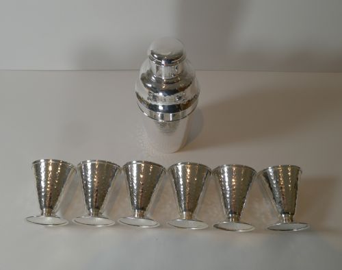 fig 2. An Art Deco silver-plated cocktail shaker set with a hammered texture, featuring a central shaker flanked by six matching flared goblets.