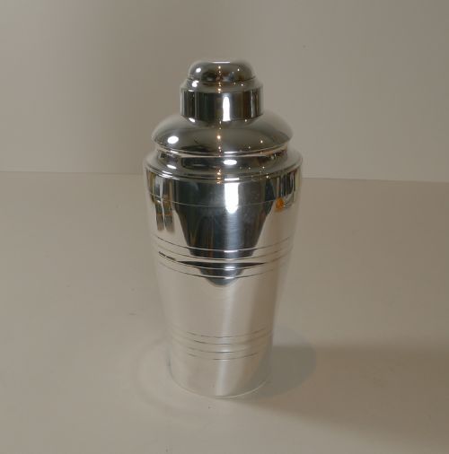 fig 1. A silver-plated Art Deco cocktail shaker displayed alongside its detached floral-embossed lemon reamer lid and small cap.