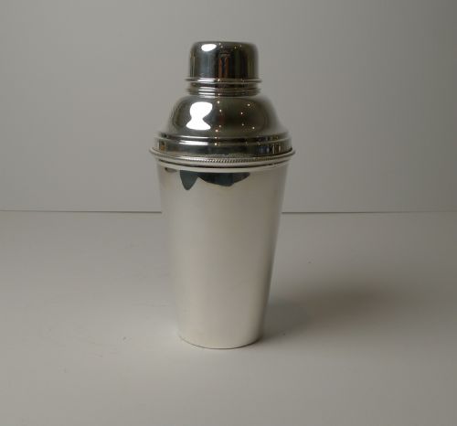 fig 1. A polished silver-plated cocktail shaker shown disassembled with its cap and integrated lemon squeezer attachment.