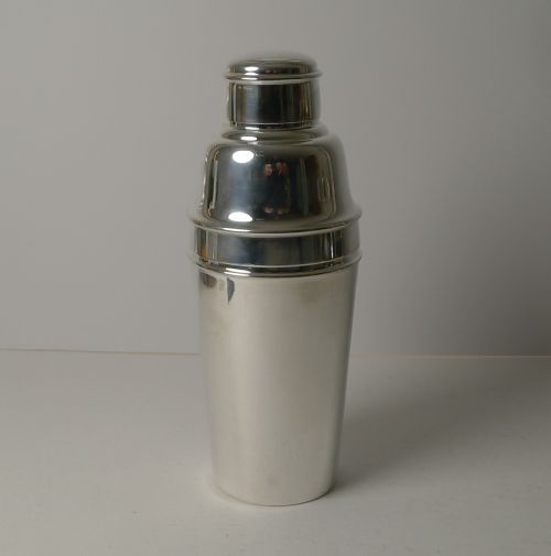 fig 1. An Art Deco silver-plated cocktail shaker presented disassembled, showing the main body, cap, and strainer lid with an integrated internal ice breaker mechanism.