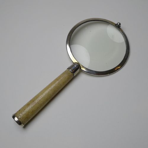 fig 2. An Art Deco handheld magnifying glass featuring a circular glass lens in a sterling silver frame attached to a tan shagreen handle.