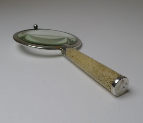 fig 3. An Art Deco handheld magnifying glass featuring a circular glass lens in a sterling silver frame attached to a tan shagreen handle.