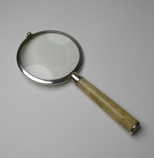 fig 4. An Art Deco handheld magnifying glass featuring a circular glass lens in a sterling silver frame attached to a tan shagreen handle.