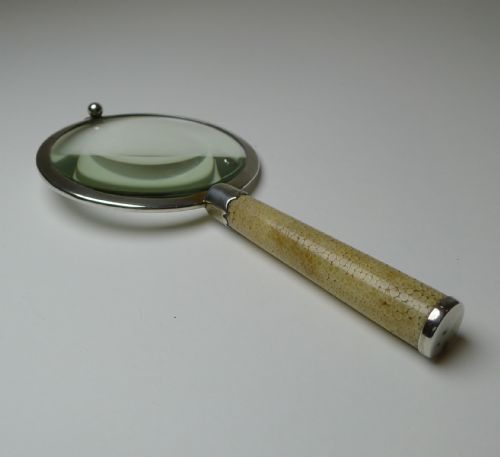 fig 5. An Art Deco handheld magnifying glass featuring a circular glass lens in a sterling silver frame attached to a tan shagreen handle.