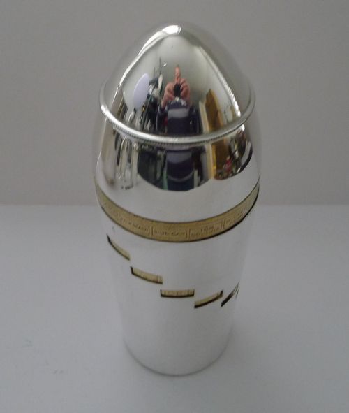 fig 1. A bullet-shaped silver-plated cocktail shaker featuring a rotating brass band and cut-out windows displaying recipe ingredients.
