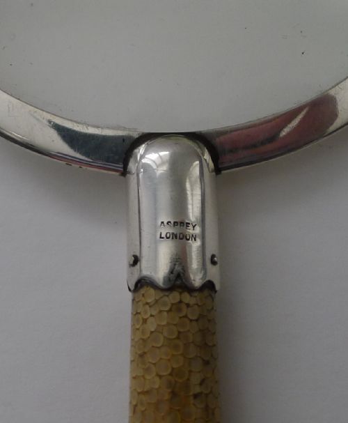 fig 1. An Art Deco handheld magnifying glass featuring a circular glass lens in a sterling silver frame attached to a tan shagreen handle.
