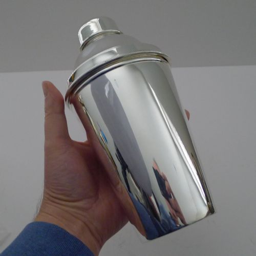fig 1. A polished silver-plated cocktail shaker displayed in three sections alongside its integrated citrus reamer lid and cap.